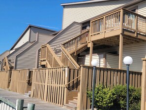 Une terrasse en bois menant à un bâtiment doté de plusieurs balcons et d’un escalier.