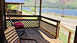 Um deck de madeira com duas cadeiras e uma mesa, com vista para um lago e colinas.