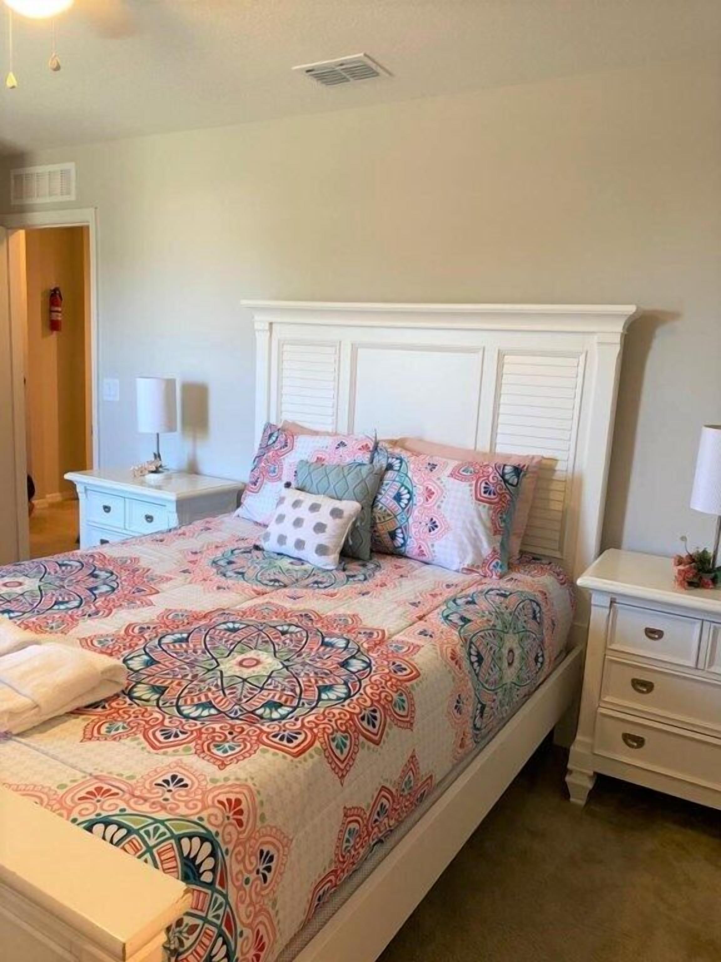 A bedroom with a bed, nightstands, a dresser, and a door.