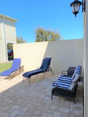 A patio area with three lounge chairs, a small table, and a wall-mounted lamp. - Compass Bay by CozyKey (Kissimmee)