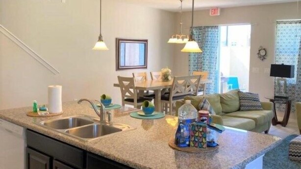 A modern kitchen with granite countertops, dark cabinetry, and pendant lighting. - Compass Bay by CozyKey (Kissimmee)