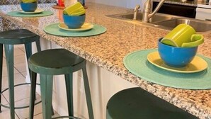 A kitchen with a granite countertop, green bar stools, and a stainless steel sink. - Compass Bay by CozyKey (Kissimmee)