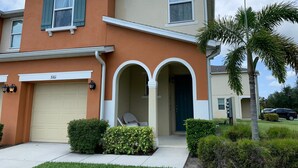 A two-story house with a garage, a covered porch with a door, and a palm tree in the front yard. - Compass Bay by CozyKey (Kissimmee)