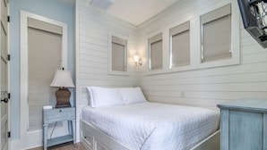 A bedroom with a white bed, a nightstand with a lamp, and a dresser. - Carriage House!  STEPS from Rosemary Tennis Courts! (Inlet Beach)