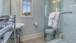 A bathroom with a glass shower enclosure, a white toilet, a sink with a chrome faucet, and a window with a view of greenery outside. - Carriage House!  STEPS from Rosemary Tennis Courts! (Inlet Beach)