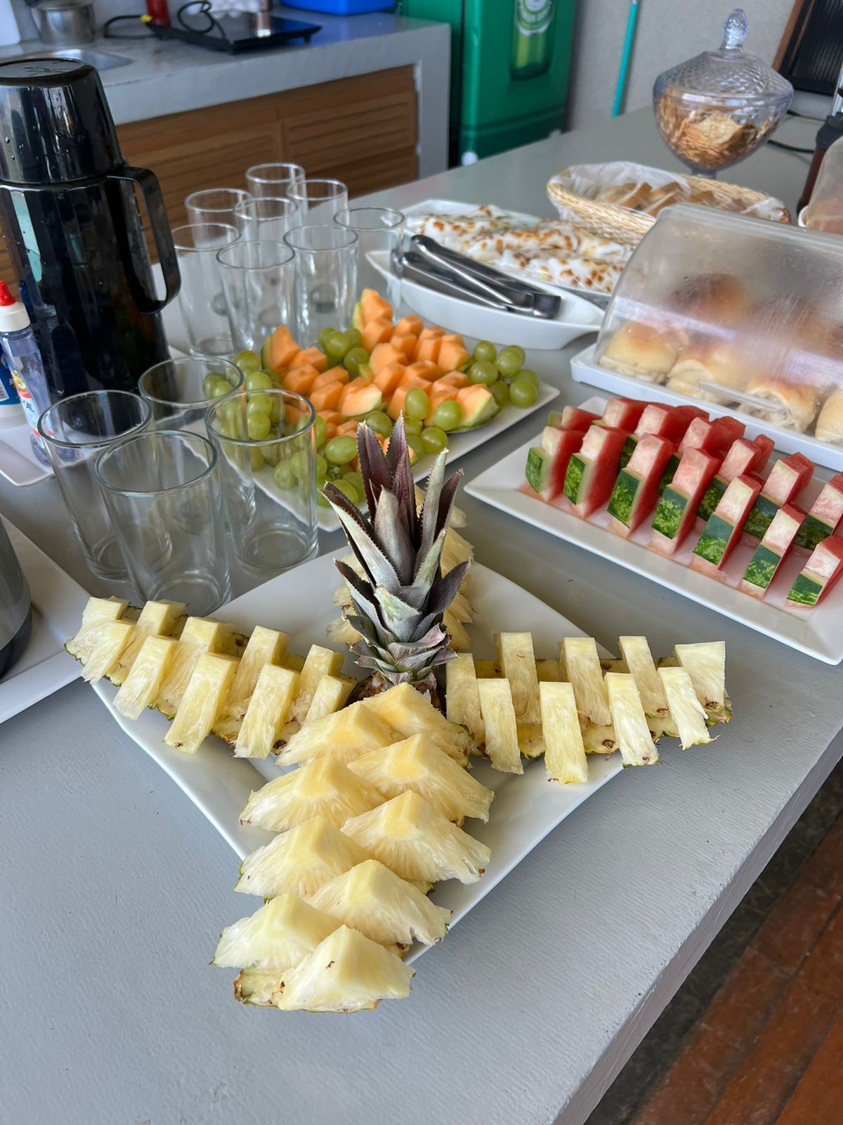 Una mesa de buffet con diversos alimentos, incluyendo piña en rodajas, uvas, melón y sándwiches.