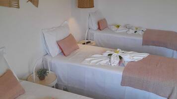 Two beds with white linens and pink accents, complemented by a small side table and woven wall hangings.
