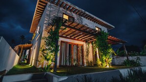 A modern two-story house with a sloped roof, wooden beams, and a well-lit entrance. - Vila Mistral pousada em São Miguel do Gostoso/RN (Touros)