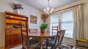 Un coin repas comprenant une table en bois, des chaises, un lustre, un vase avec des fleurs et une fenêtre avec des rideaux.