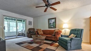 Un salon avec un ventilateur de plafond, un canapé, un fauteuil, une table basse et une lampe.