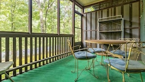 Un espace extérieur abrité, avec une table et des chaises, un tapis vert et une vue sur les arbres.