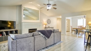 A living room with a gray sofa, a fireplace, a dining area with a table and chairs, and a ceiling fan. - 18932 - 32 Belleza Way (Hot Springs Village)