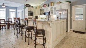 Een ruime keuken met witte kasten, een groot eiland en een eethoek met houten stoelen.