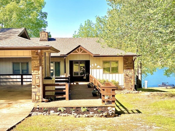 A two-story house with a stone facade, a front porch, and a view of a lake.