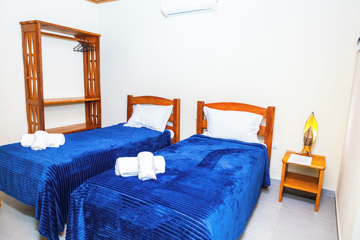 Une chambre d’hôtel avec deux lits, chacun recouvert d’une courtepointe bleue et agrémenté d’oreillers blancs, une tête de lit en bois et une petite table de chevet avec une lampe.