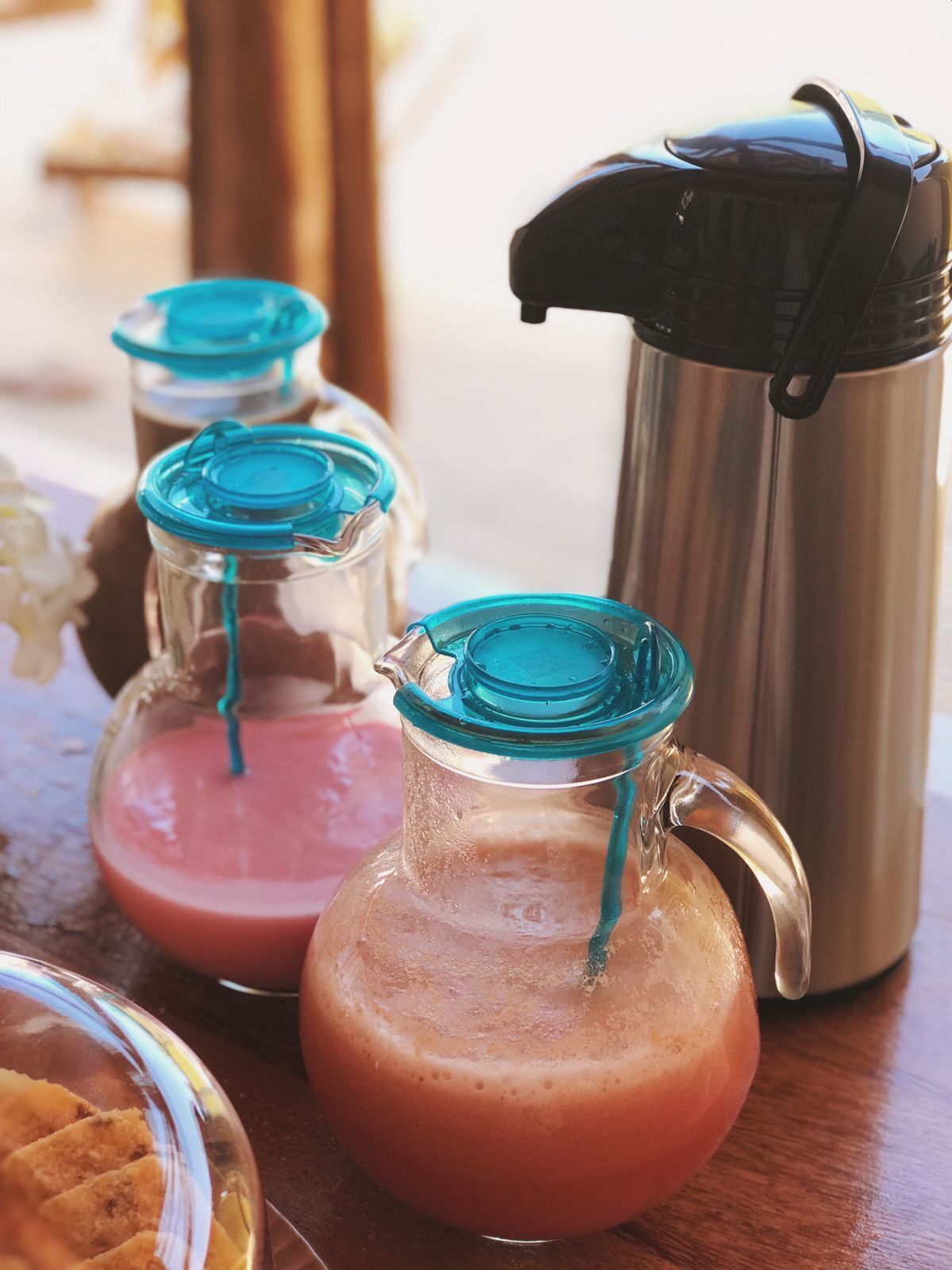 Three glass bottles with blue lids, a stainless steel thermos, and a glass pitcher on a wooden table.