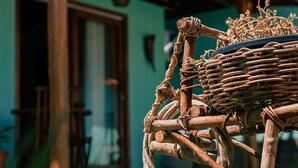 A rustic wooden cart with a woven basket, set against a house with a green door and a window. - Pousada Villa Kai  (São Miguel dos Milagres)