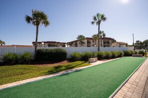A golf course with a green fairway, a white fence, and palm trees.