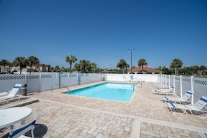 A rectangular pool with a white fence, lounge chairs, and a table.