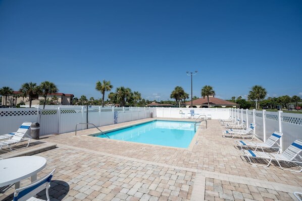 A rectangular pool with a white fence, lounge chairs, and a table.