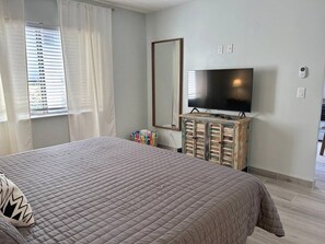 A bedroom with a large bed, a television on a wooden cabinet, and a window with blinds.