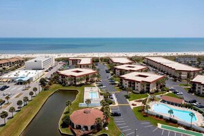 A beachfront hotel with multiple buildings, a swimming pool, and a parking lot.