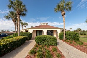 A building with a red-tiled roof, surrounded by palm trees and well-maintained hedges.