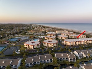 A coastal hotel complex with multiple buildings, a swimming pool, and a view of the beach.