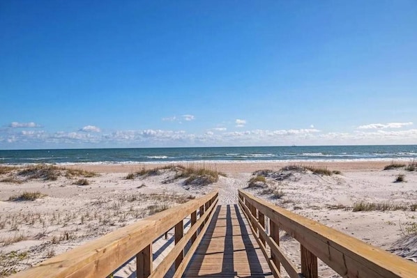 A wooden boardwalk leading to a beach with dunes and ocean in the background.