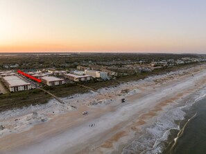 An aerial view of a coastal area with a beachfront hotel complex, sandy beach, and ocean.