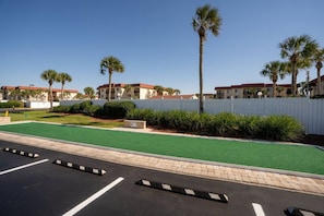 A parking lot with green artificial turf, a white picket fence, and palm trees.