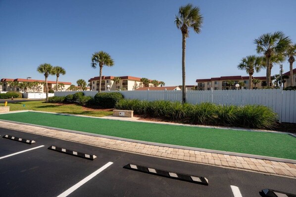 A parking lot with green artificial turf, a white picket fence, and palm trees.