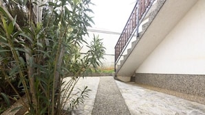 Een verhard pad met een middenberm, omzoomd door beplanting en een gebouw met een witte gevel en een stenen basis.