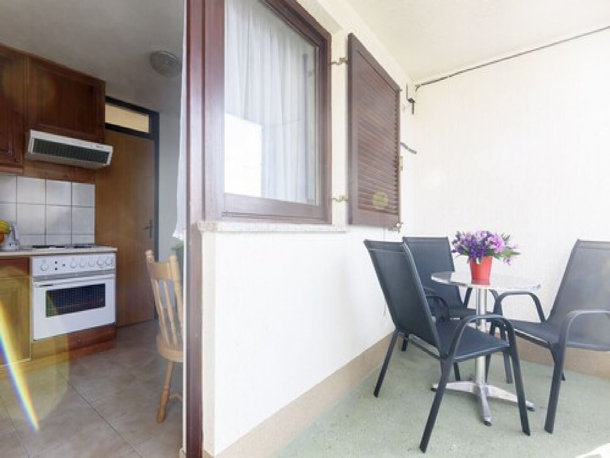 A small balcony with a table and chairs, a potted plant, and a view of a kitchen area with a stove and cabinets.