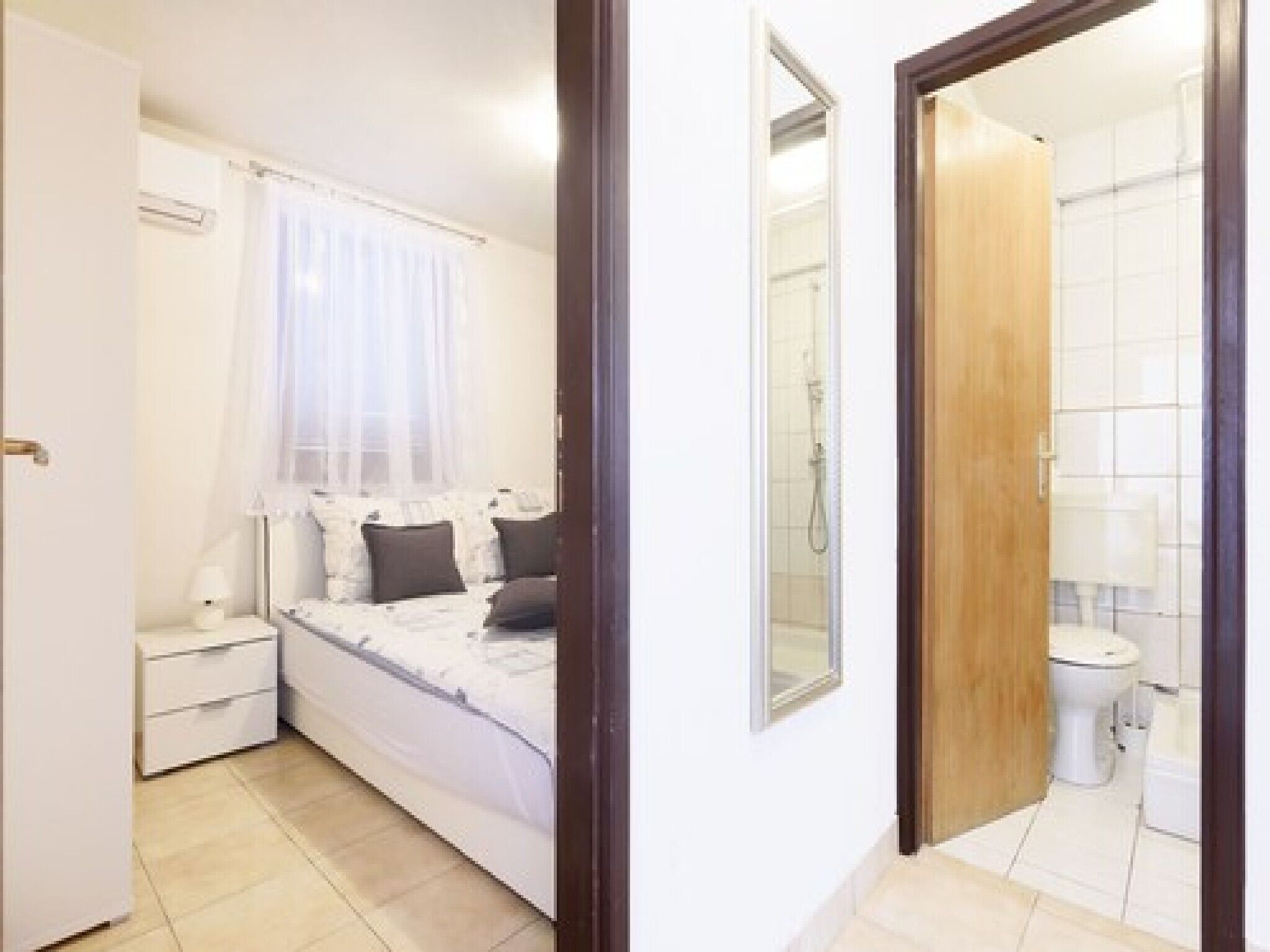 Quarto com cama, mesa de cabeceira e janela com cortinas leves.