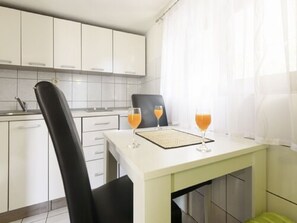 A modern kitchen with white cabinets, a black chair, and two glasses of orange juice on a table. - Apartments Papilon - One Bedroom Apartment with Terrace (Karin Gornji)