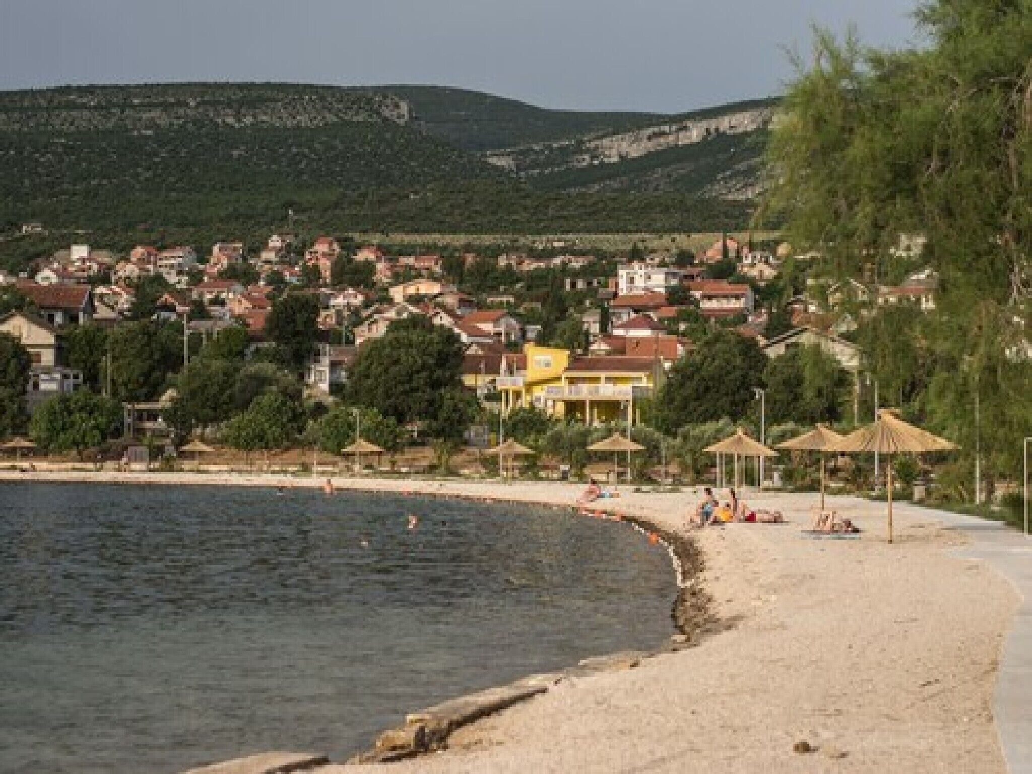 A coastal town with a sandy beach, houses, and a hilly backdrop.