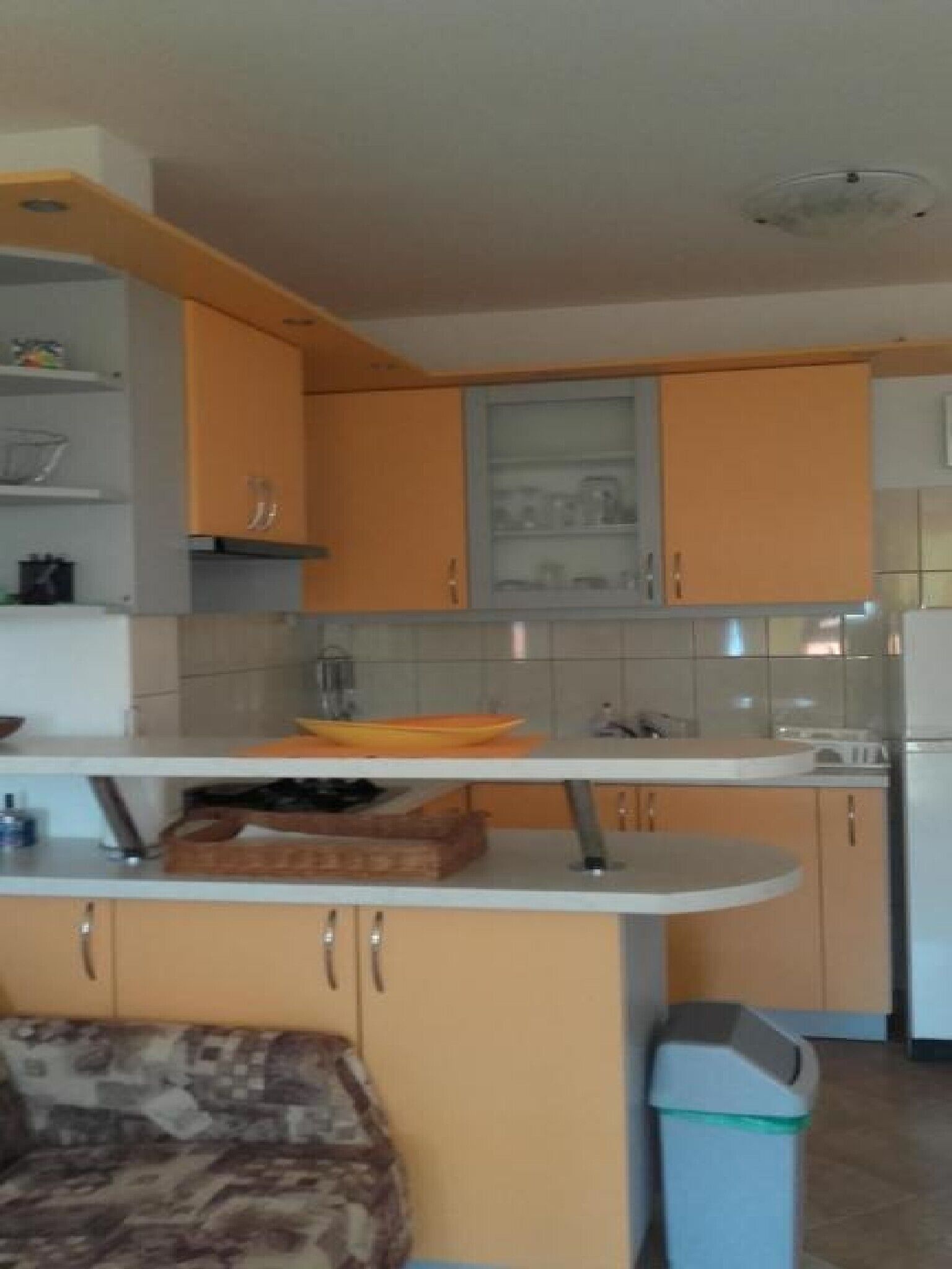 A kitchen with orange cabinets, a white countertop, and a trash bin.