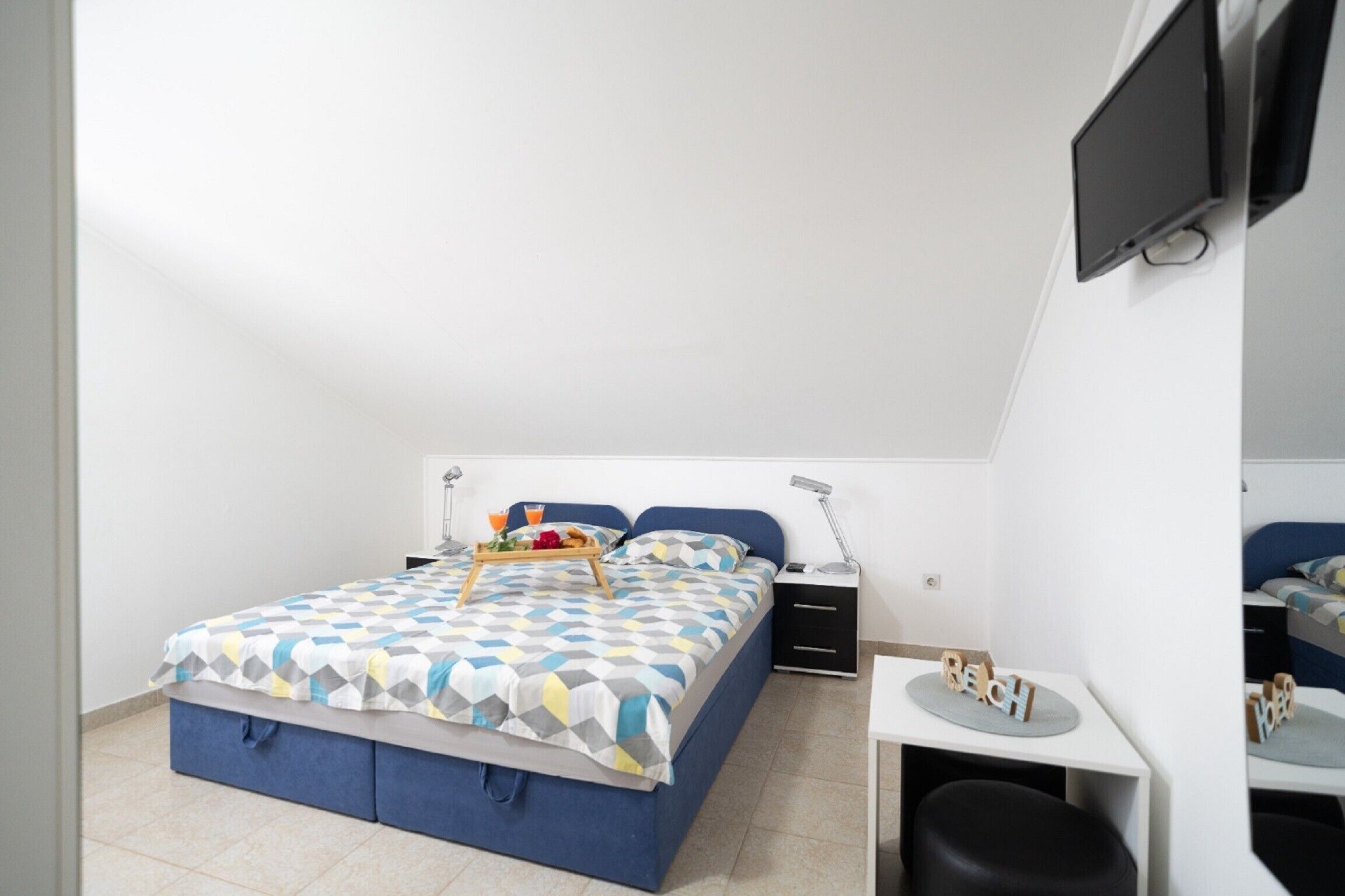 Un dormitorio con cama, mesitas de noche, un escritorio y un televisor montado en la pared.