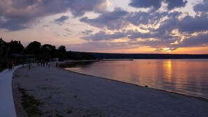 Una playa con mar tranquilo, un atardecer de fondo y algunas personas caminando por la orilla.
