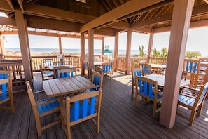 Eine Holzterrasse mit Tischen und Stühlen mit Blick auf den Strand.