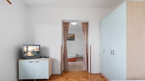 Un dormitorio con cama, televisor en un mueble, armario y puerta que da a otra habitación.
