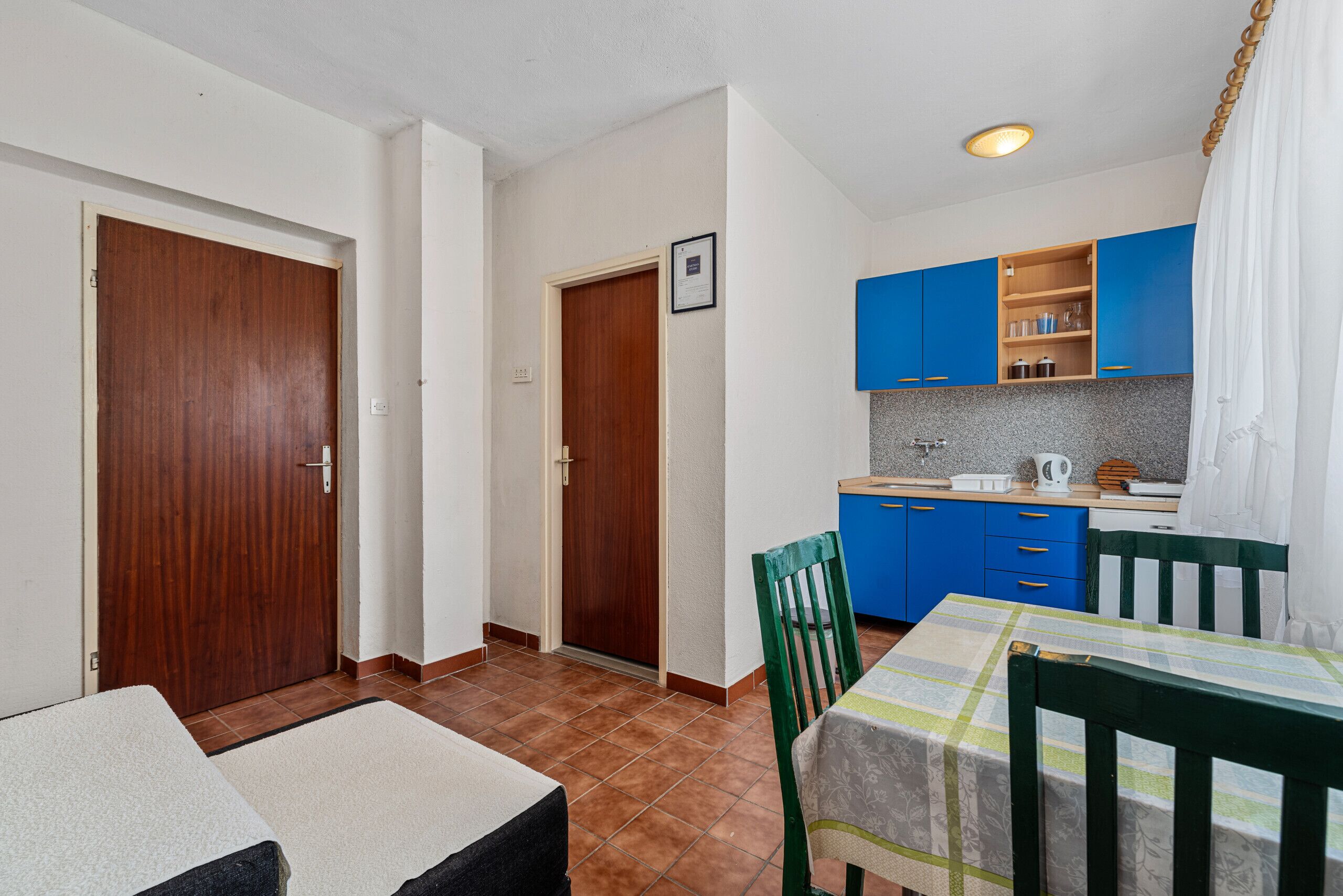 Une cuisine compacte avec des meubles bleus, un pare-feu en carrelage et un petit coin repas comprenant une table et des chaises.
