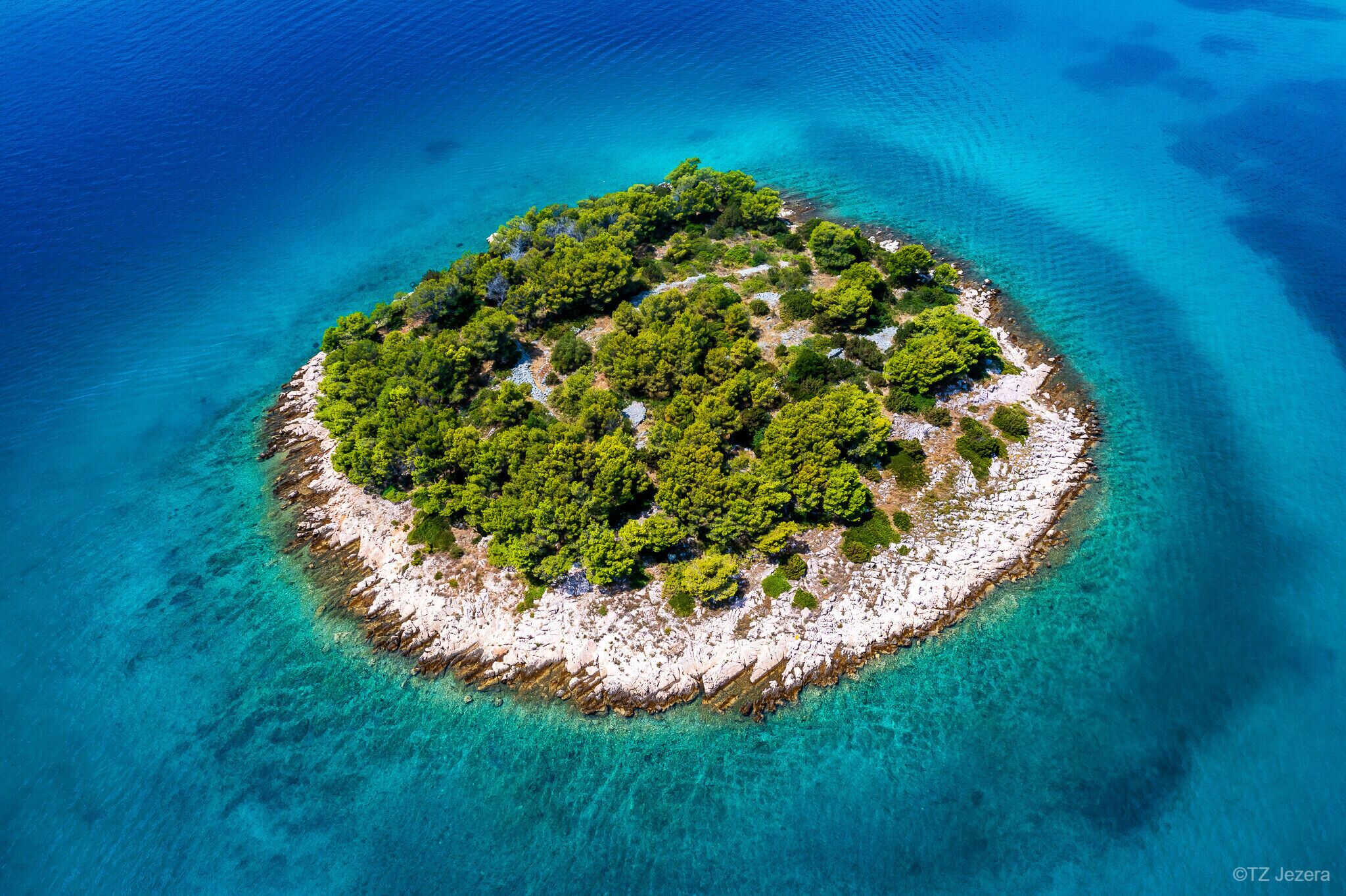 An aerial view of a small, circular island with dense green vegetation and clear turquoise waters surrounding it.