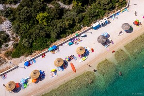 Vista aérea de uma praia com guarda-sóis, cadeiras de praia e um mar azul cristalino.