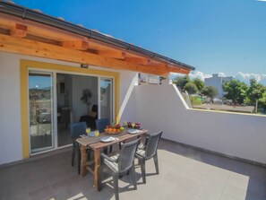 Un balcon avec une table et des chaises en bois, une porte vitrée donnant sur l’intérieur et une vue sur les environs.