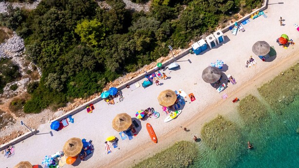 Een luchtbeeld van een strand met parasols, ligbedden en een heldere blauwe zee.