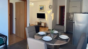 Un comedor moderno con una mesa redonda preparada para cuatro personas, un televisor en la pared y una cocina con refrigerador y armarios.