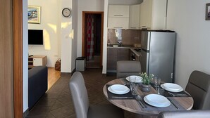 Una cocina moderna con refrigerador empotrado, un comedor con mesa redonda para cuatro, y una sala de estar con sofá y televisor.