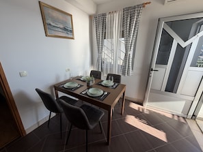Un coin repas avec une table dressée pour quatre personnes, des chaises, un tableau au mur et une porte donnant sur un beau paysage.